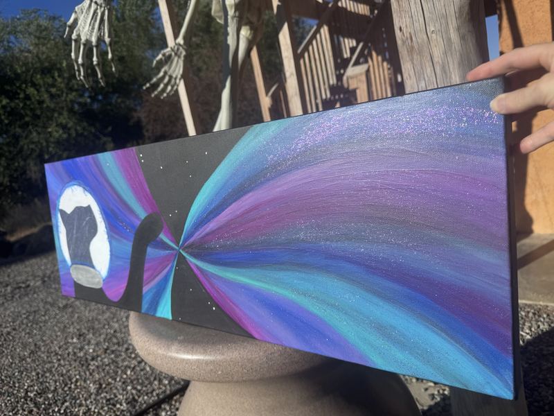 Finished wide painting of a black cat before a moon with glittering purple, blue and teal light rays, held outdoors