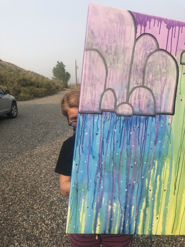Rachel peeking from behind a canvas with gray arches over blue, purple and green paint drips and tiny hearts