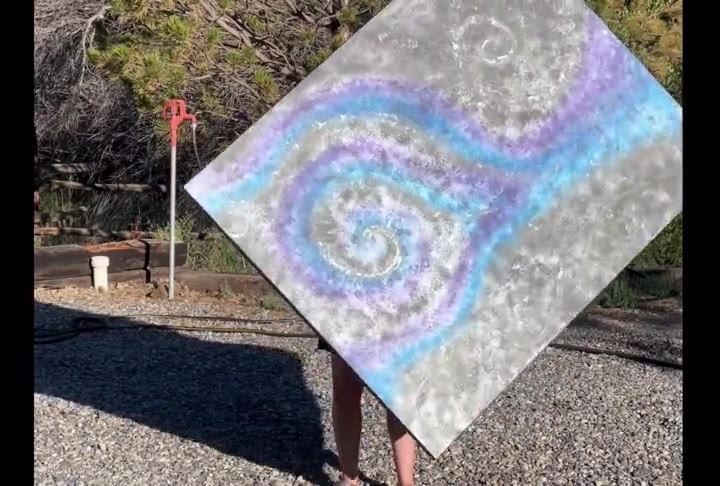 Video of a black canvas with glittery blue and purple spirals, held outdoors