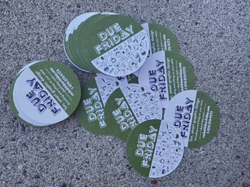 A pile of round Due Friday business cards in green and white on pavement