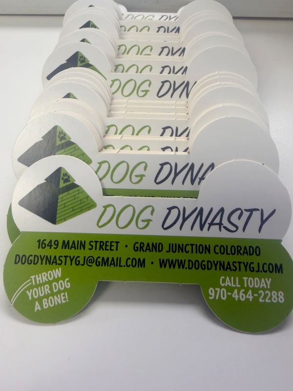 A stack of bone-shaped, cut-to-shape business cards for Dog Dynasty in green, white and navy
