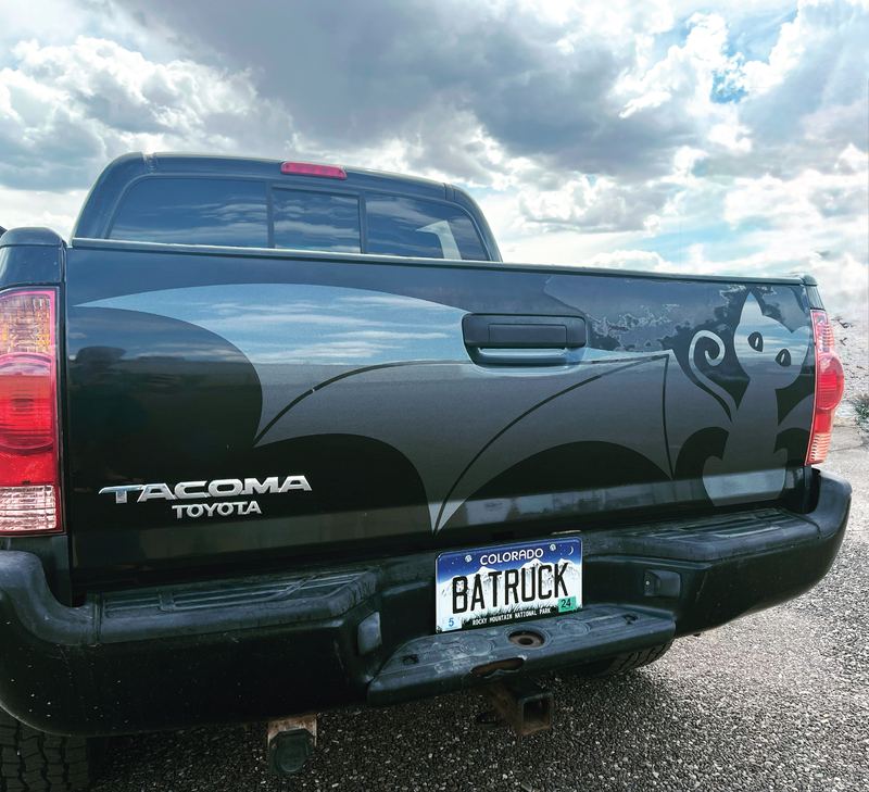 Tailgate of a black Tacoma with a large metallic cut-vinyl bat design above a BATRUCK license plate