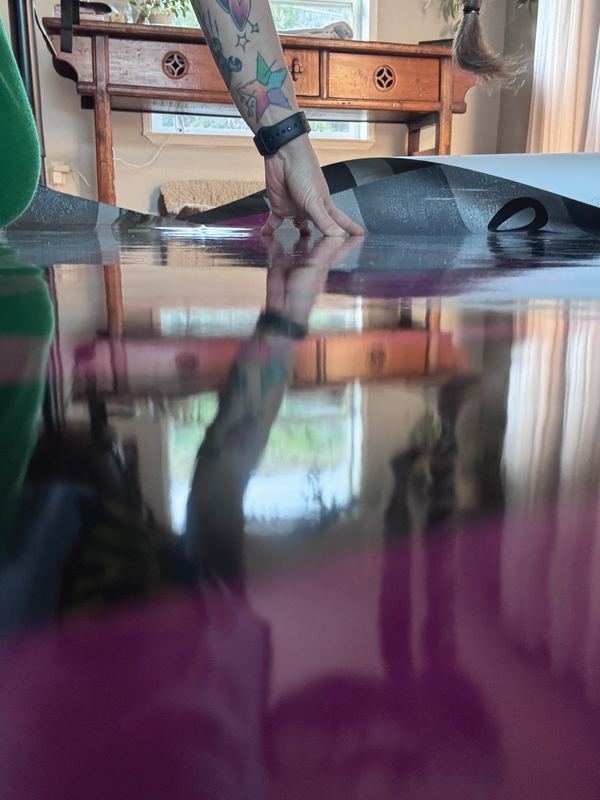 A hand smoothing a large sheet of printed wrap material, its glossy laminate reflecting the room
