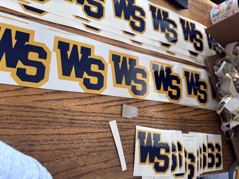 Rows of printed WS Mustangs decals laid out on a wooden table next to a pile of cut-away vinyl scraps