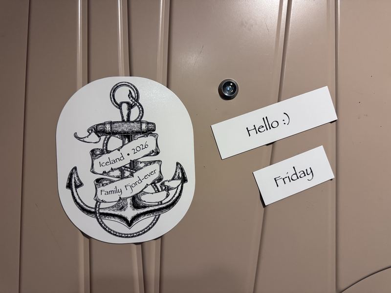 A cut-to-shape anchor magnet reading Iceland 2026 Family Fjord-ever, and two small name magnets reading Hello and Friday, on a cabin door